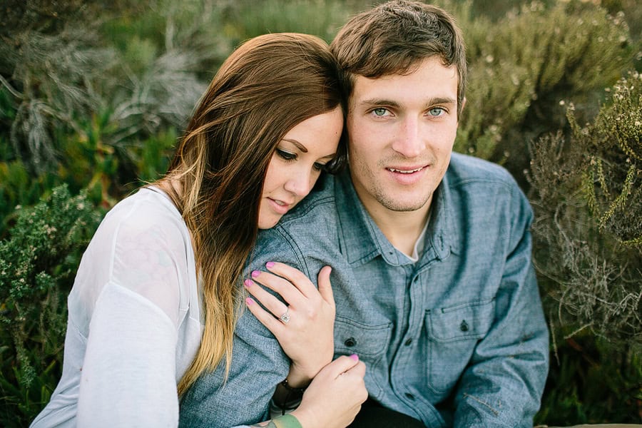 A gorgeous couple snuggled together in the greenery surrounding the beach.