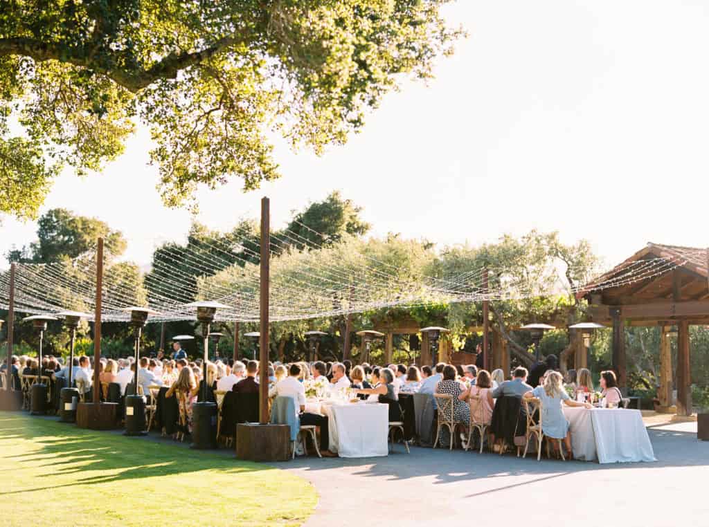 Long farmhouse tables set for a wedding reception outside with market lights strung above 