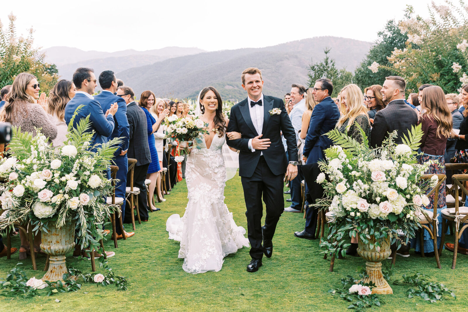 Bride and groom walk joyfully down the aisle after their wedding ceremony at Holman Ranch in Carmel, surrounded by lush florals and joyful guests.