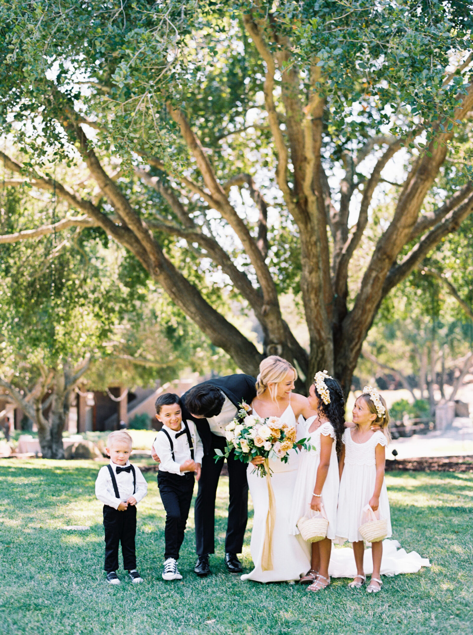 Candid moment between a bride, groom, flower girls, and ring bearers at Villa Loriana in San Luis Obispo, surrounded by lush gardens and Tuscan-inspired architecture.