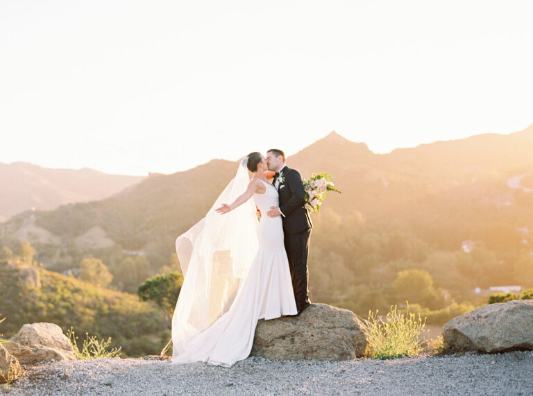 Bride and groom sunset kiss at Cielo Farms in Malibu. Sarah's veil catches the breeze as she embraces Spencer, her bouquet elegantly tucked behind his back. A romantic golden hour wedding portrait at an iconic Malibu vineyard venue.