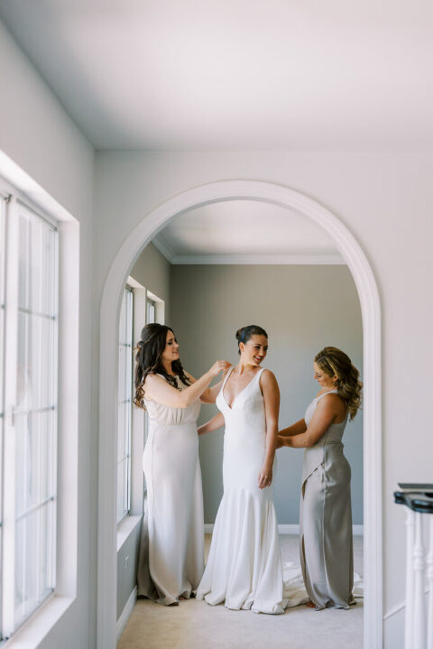 Bride getting ready with the help of her bridesmaids, capturing a classic wedding morning moment. A timeless bridal prep photo filled with laughter, love, and elegant details.