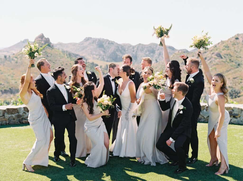 Bride and groom share a kiss as their bridal party cheers them on, celebrating their wedding day. A joyful and candid wedding moment with bridesmaids and groomsmen at Cielo Farms in Malibu.