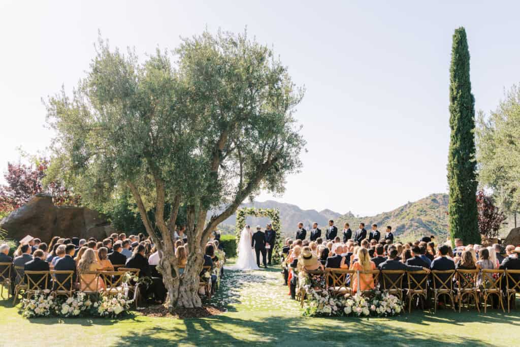 Bride and groom stand at the center of the aisle during their wedding ceremony at Cielo Farms in Malibu, surrounded by family and friends. A heartfelt moment with guests watching against the stunning backdrop of the Santa Monica Mountains.