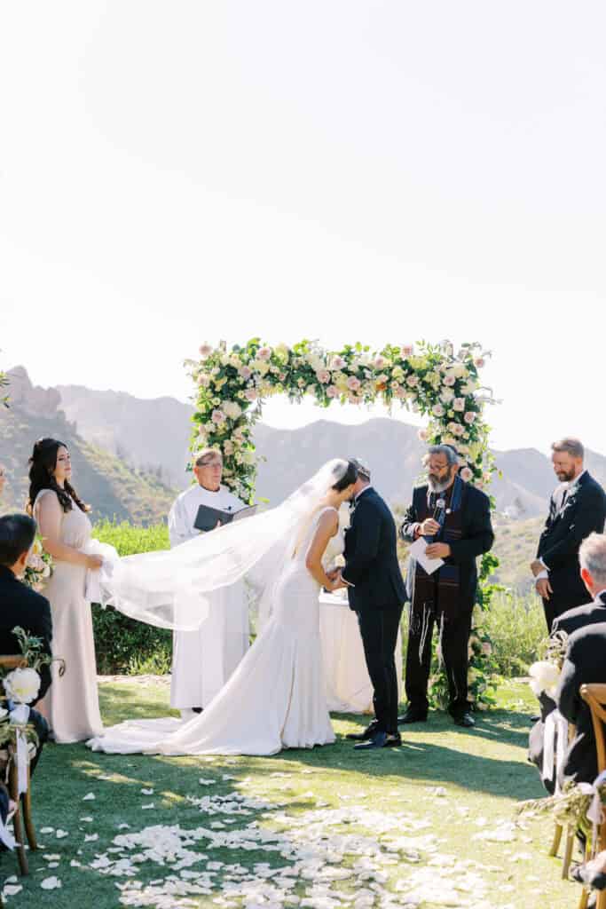 A sweet and intimate moment as the bride kisses her groom on the cheek during their wedding ceremony at Cielo Farms in Malibu, with the Santa Monica Mountains as a stunning backdrop.