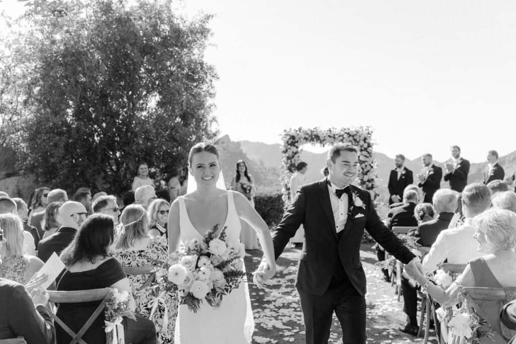 A joyful black and white photo capturing the newlyweds as they walk back down the aisle at Cielo Farms in Malibu, just pronounced husband and wife, with guests cheering in celebration.
