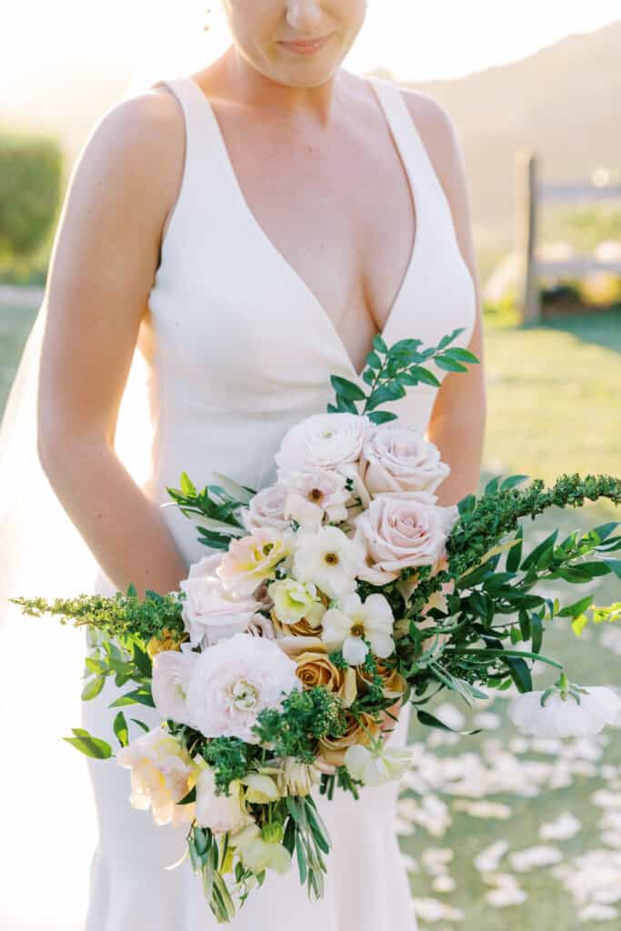 Close-up photo of the bride holding her bridal bouquet by Bella Blooms, featuring a soft romantic color palette of pastel blooms. Elegant wedding flowers captured in natural light.