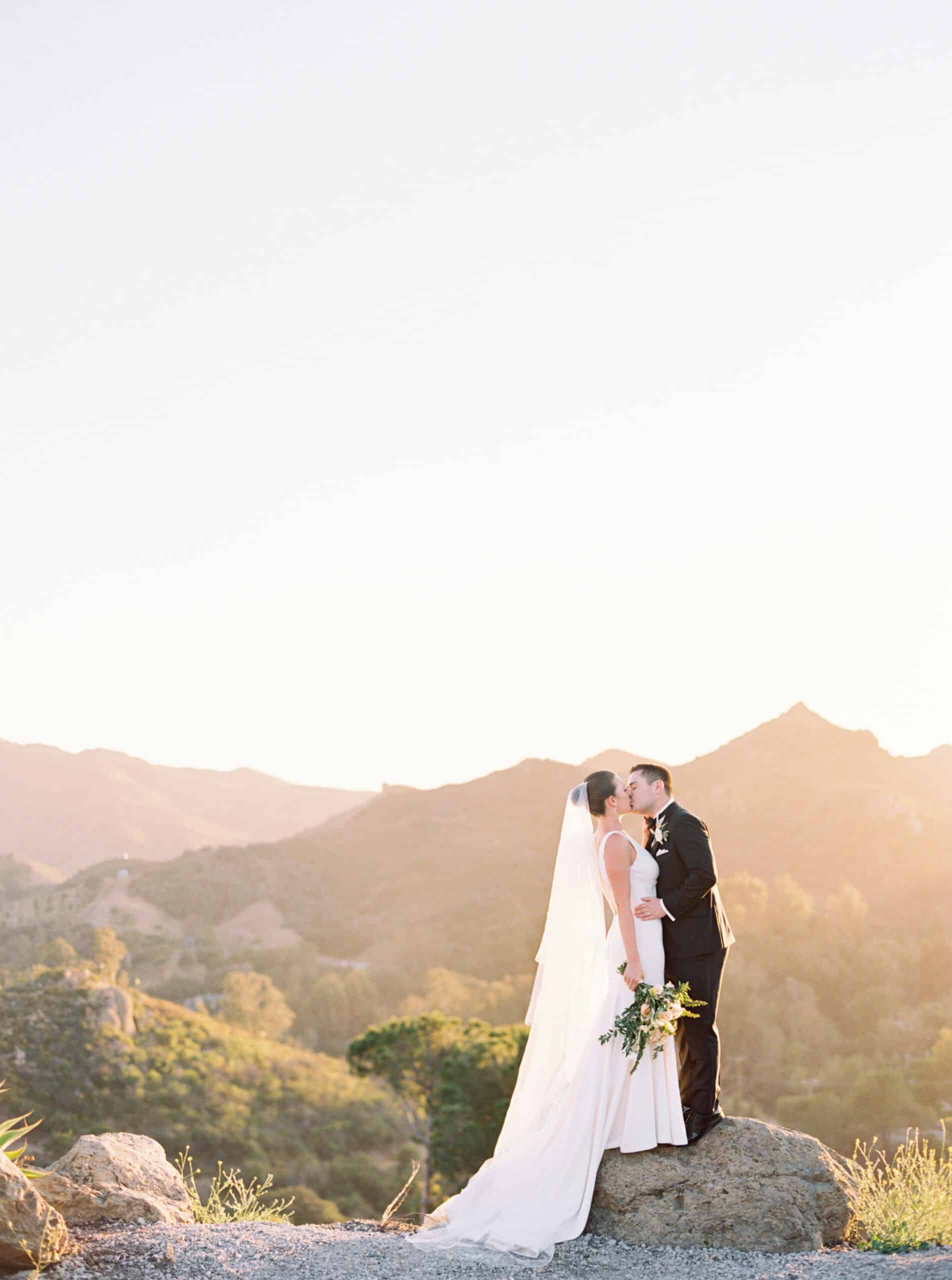 A stunning portrait of the bride and groom sharing a kiss with the Santa Monica Mountains in the background and the warm glow of the setting sun at Cielo Farms in Malibu.