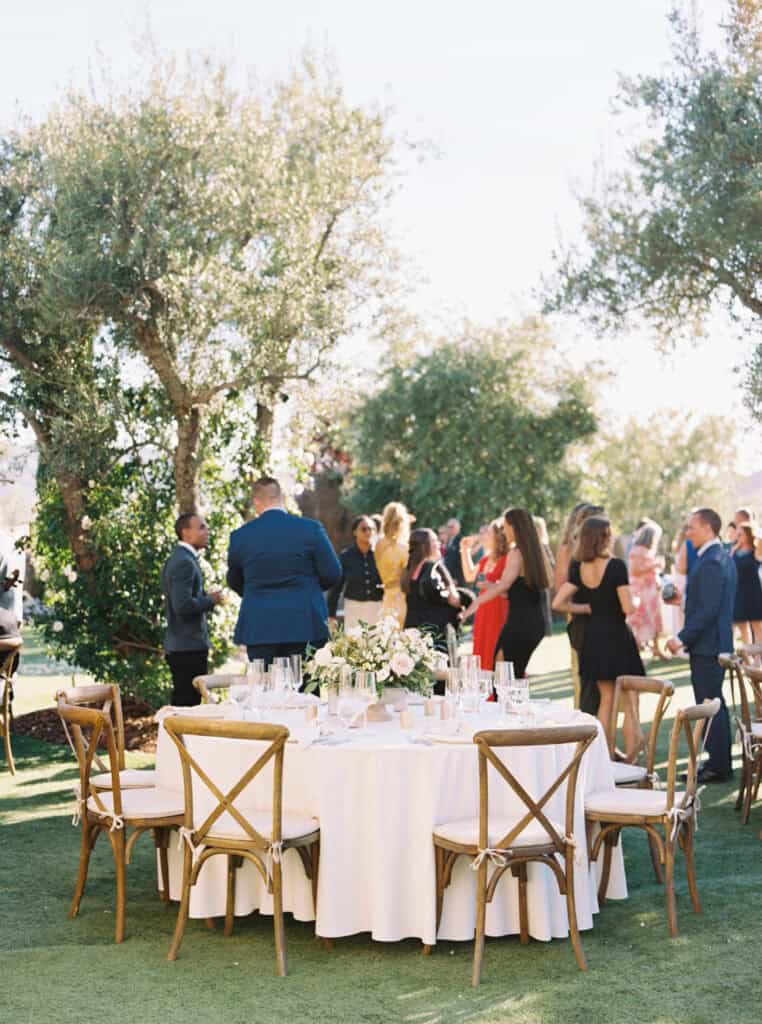 A beautifully set reception table at Cielo Farms, featuring a soft white linen tablecloth, romantic pastel floral arrangement, and elegant wooden cross-back chairs for a luxurious wedding celebration.