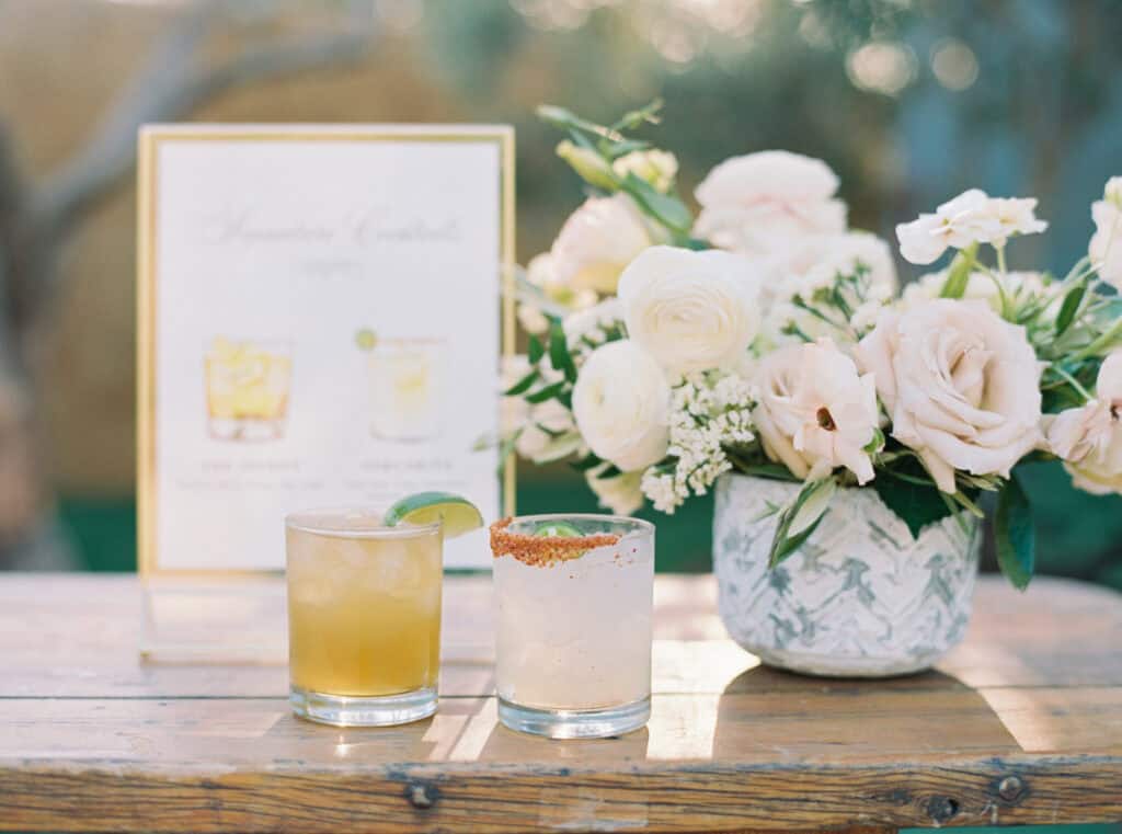 The bride and groom’s signature cocktails at their wedding, displayed with a custom bar sign and a beautiful floral arrangement at Cielo Farms, offering a personalized and elegant touch to the celebration.