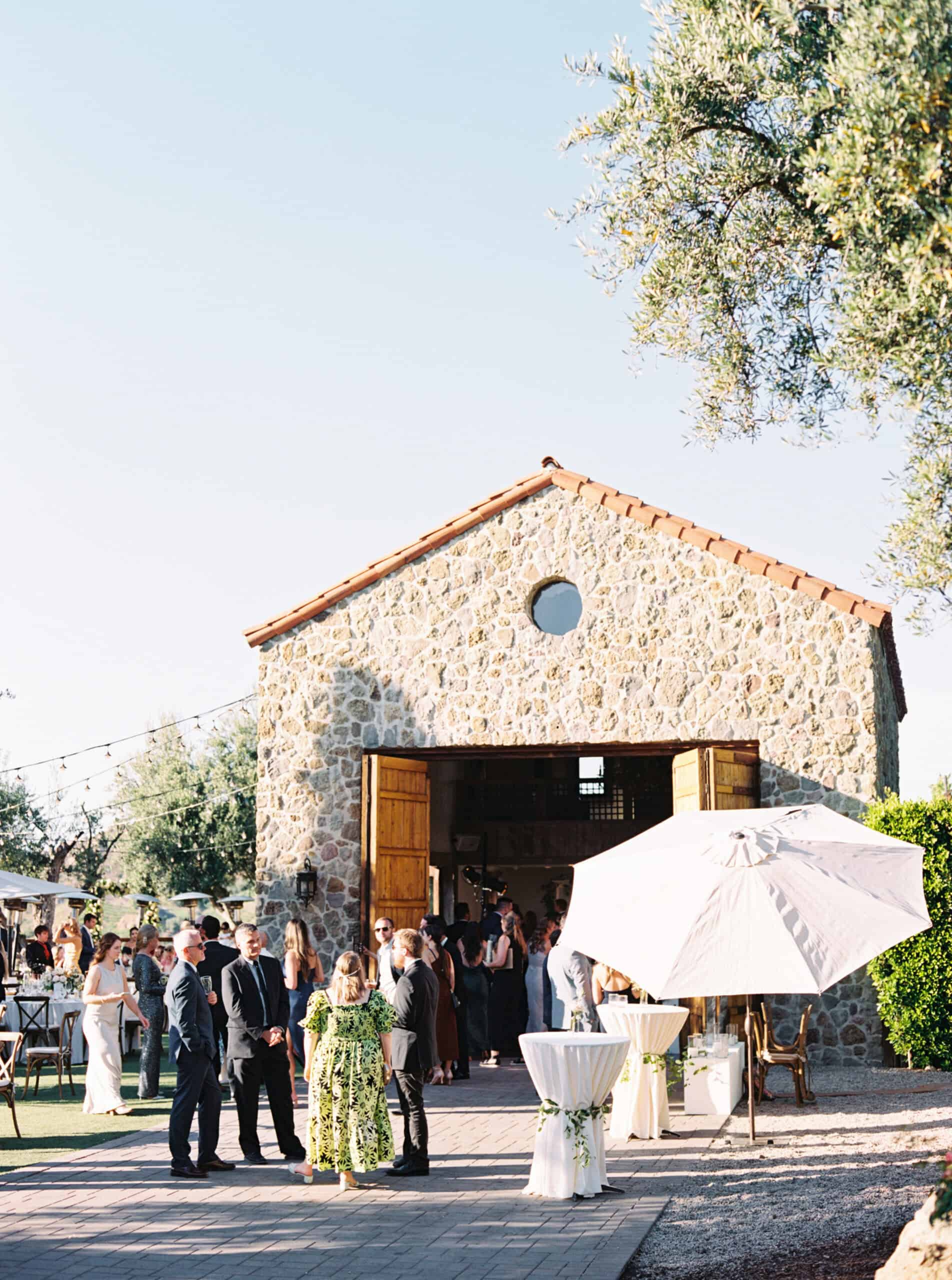 Guests enjoy cocktail hour at Cielo Farms, with the iconic stone building as a stunning backdrop during their Malibu wedding celebration.