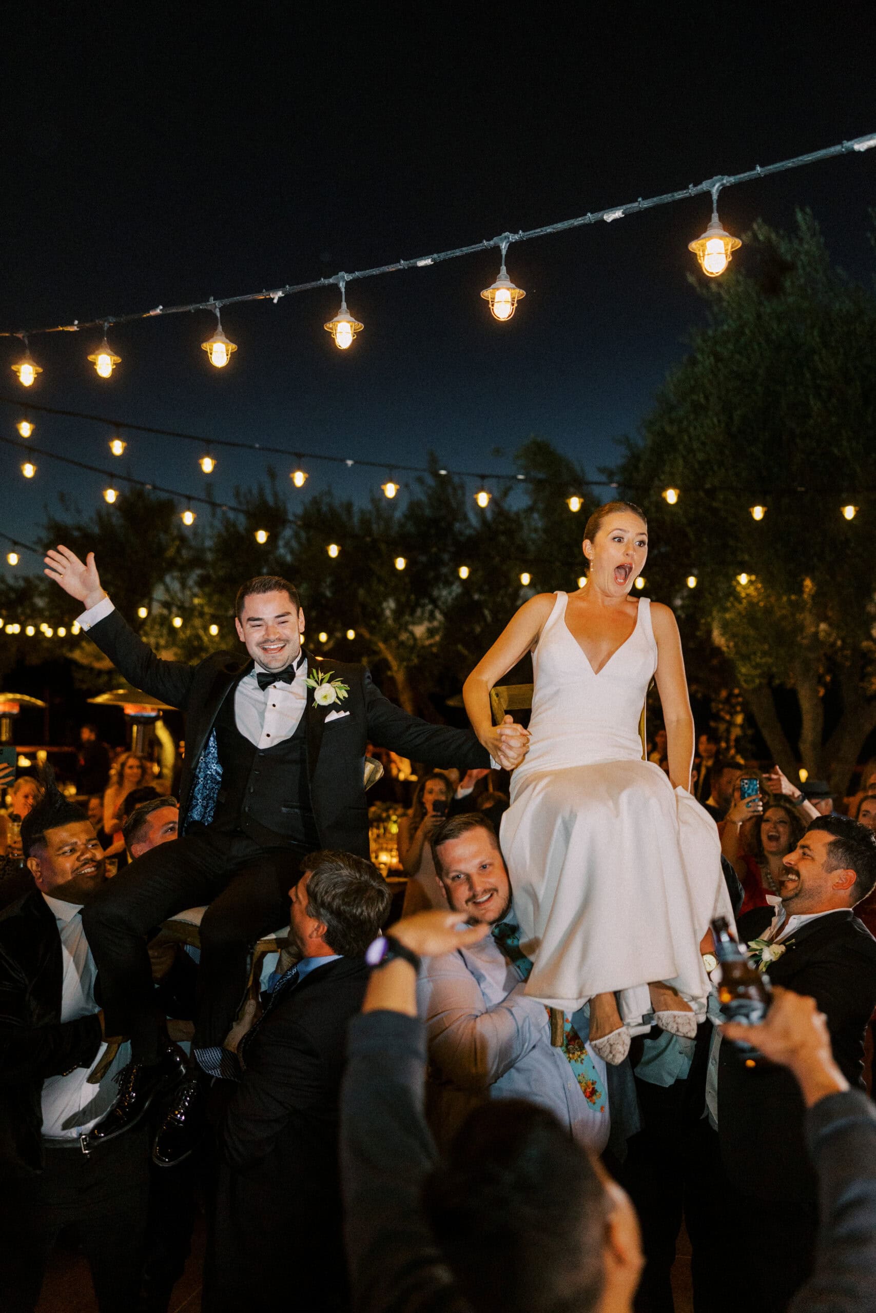 Guests lift the bride and groom on chairs during the wedding celebration, honoring the Jewish tradition of the Hora dance at Cielo Farms, filled with joy and lively energy.