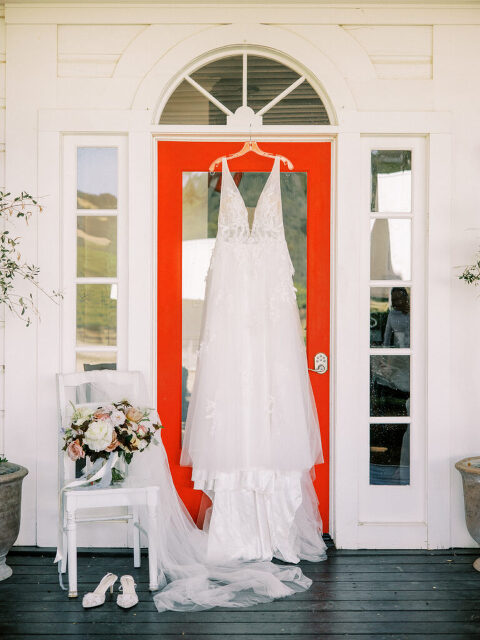 The bride’s wedding dress hangs on the iconic red door of the Hammersky Vineyards farmhouse, with her shoes and bouquet nearby.