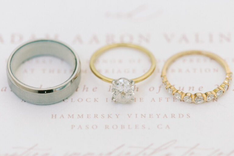 A close-up photo of the couple’s wedding rings placed on their invitation, highlighting the name of their wedding venue, Hammersky Vineyards.