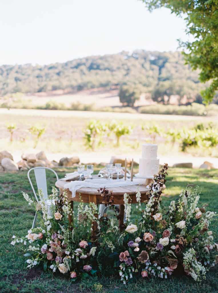 A sweetheart table at Hammersky Vineyards adorned with lush florals, elegant white metal chairs, and a simple two-tiered wedding cake.