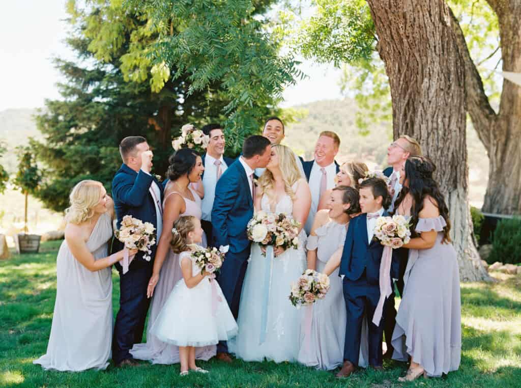 The full bridal party cheers as the newlyweds share a joyful kiss, celebrating their love at Hammersky Vineyards.