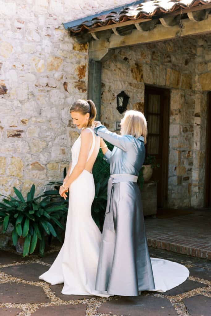 The mother of the bride helps her daughter into her wedding dress in the courtyard at Holman Ranch.