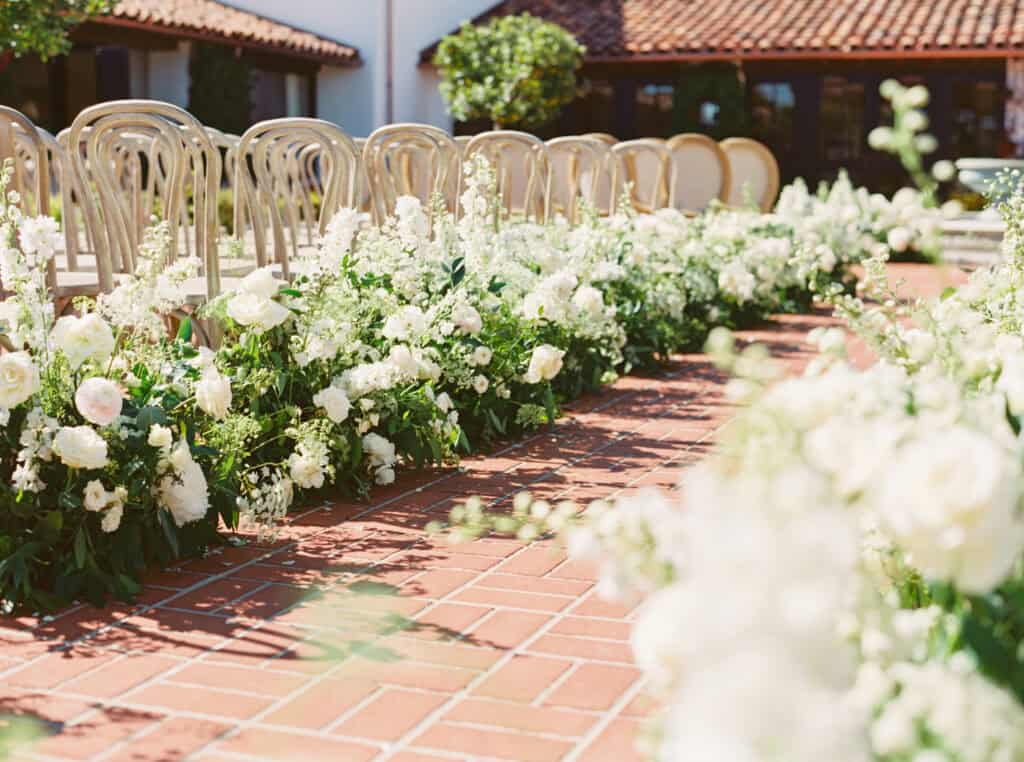 A close-up view of a lush white floral arrangement lining the wedding ceremony aisleway.