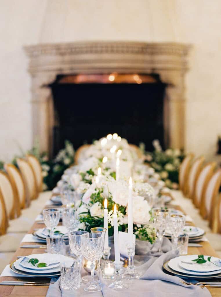 A long reception table fully set and ready for guests at Laura and Matt's Pebble Beach wedding, featuring candlelight, layered china, custom menus, and crystal glassware, designed by Charmed Events.