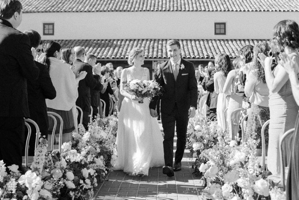 A classic black and white photo of the newlyweds walking down the aisle after being pronounced husband and wife at the Monterey Peninsula Country Club in Pebble Beach.