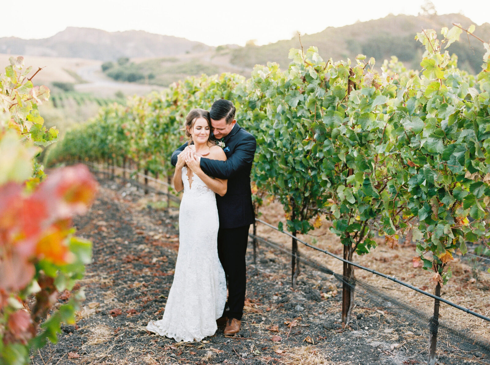 A groom wraps his arms around his bride as they stand in the vineyards at Greengate Ranch in San Luis Obispo.