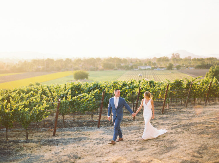 Bride and Groom walk hand in hand past the vineyards at Greengate Ranch during their San Luis Obispo wedding. Captured at sunset, the golden glow creates a romantic and timeless moment at this stunning Central Coast wedding venue.