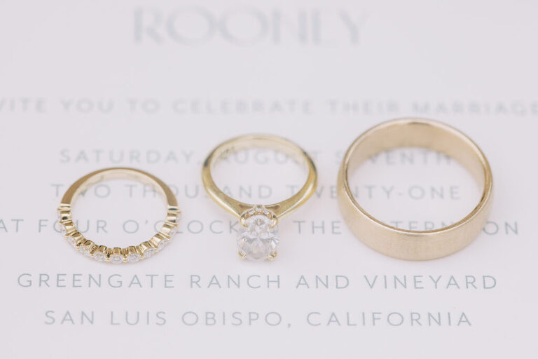 A close-up of Michelle and Brendan’s wedding rings elegantly placed on their white invitation, highlighting Greengate Ranch & Vineyards as the venue for their San Luis Obispo wedding.