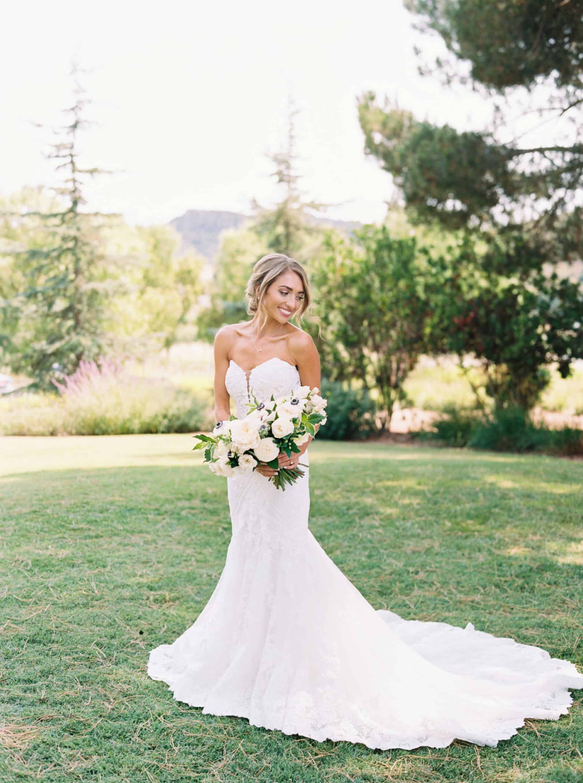 Bride Michelle radiates elegance in a full-length portrait outside the Ranch House at Greengate Ranch, showcasing her strapless lace wedding dress, timeless updo, and classic all-white bouquet.