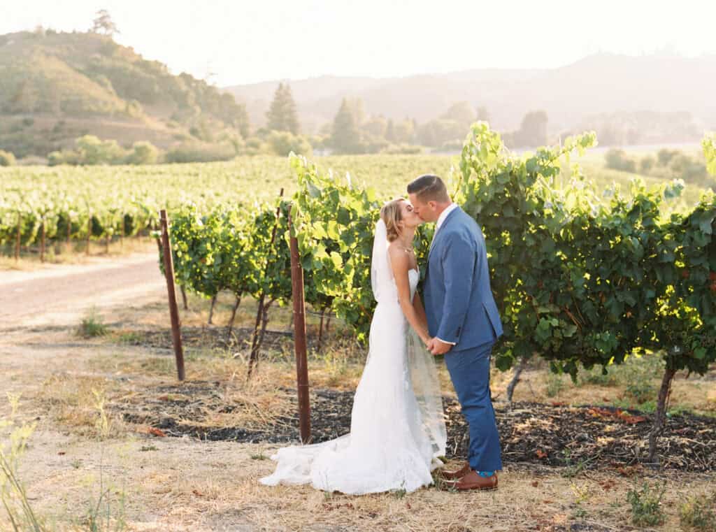 Michelle and Brendan share a kiss in the picturesque vineyards at Greengate Ranch during sunset, capturing a romantic and serene moment away from the reception.