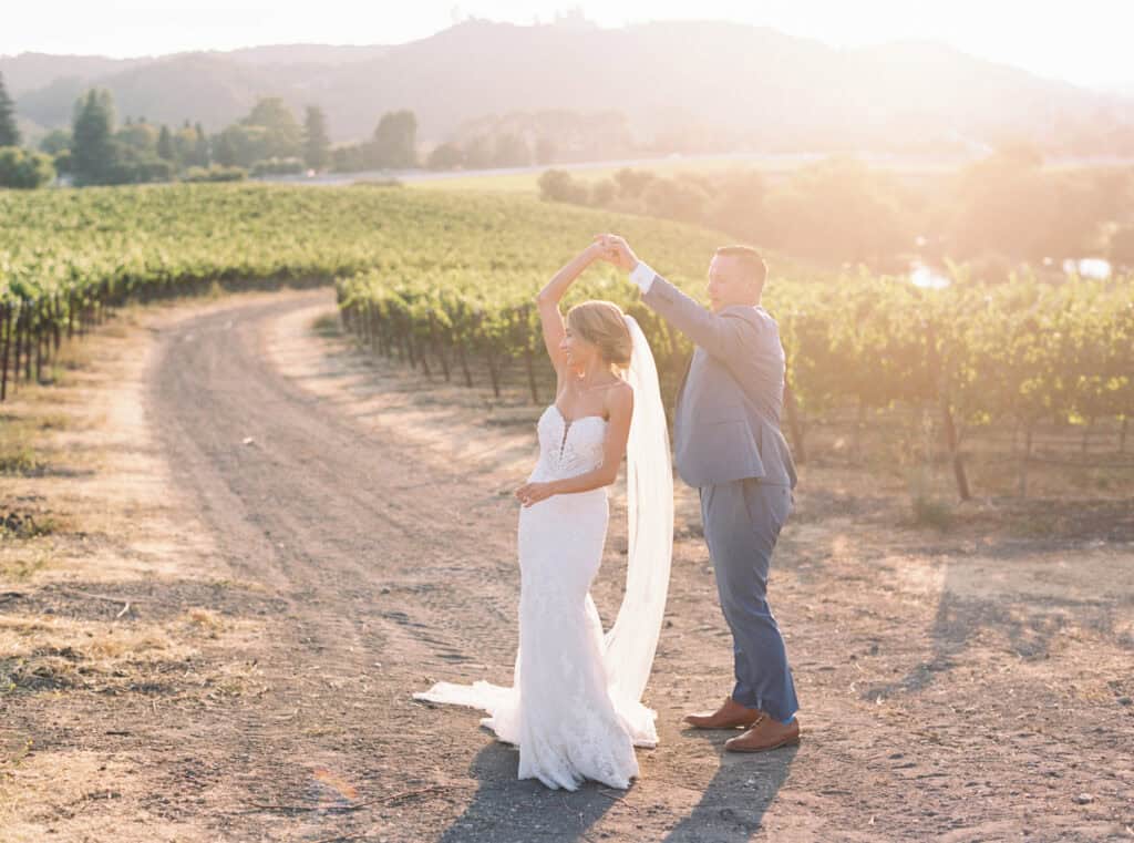 Brendan twirls his wife, Michelle, in a joyful moment during their sunset photos at Greengate Ranch, surrounded by the lush vineyards, capturing their playful and romantic celebration.