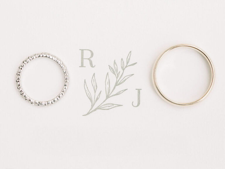 A close-up detail shot of wedding rings placed on a custom wedding invitation, featuring the couple’s initials, at a private estate wedding in Lodi, CA.