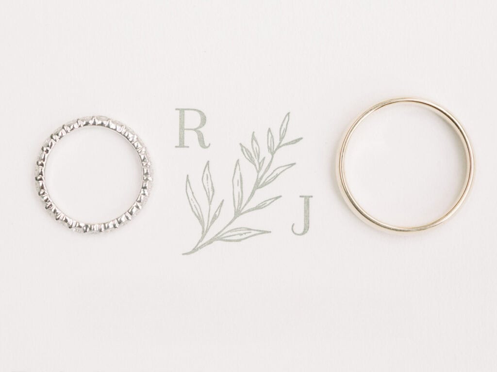 A close-up detail shot of wedding rings placed on a custom wedding invitation, featuring the couple’s initials, at a private estate wedding in Lodi, CA.
