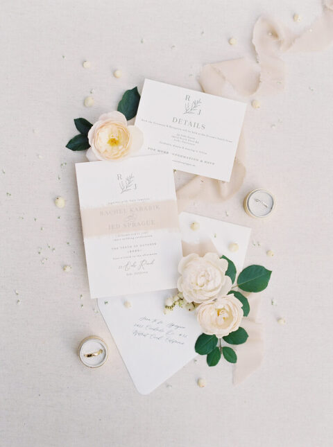 A styled flat lay of the wedding invitation suite, featuring soft white and pink roses, delicate ribbon, and the couple’s wedding bands at their private estate wedding in Lodi, CA.