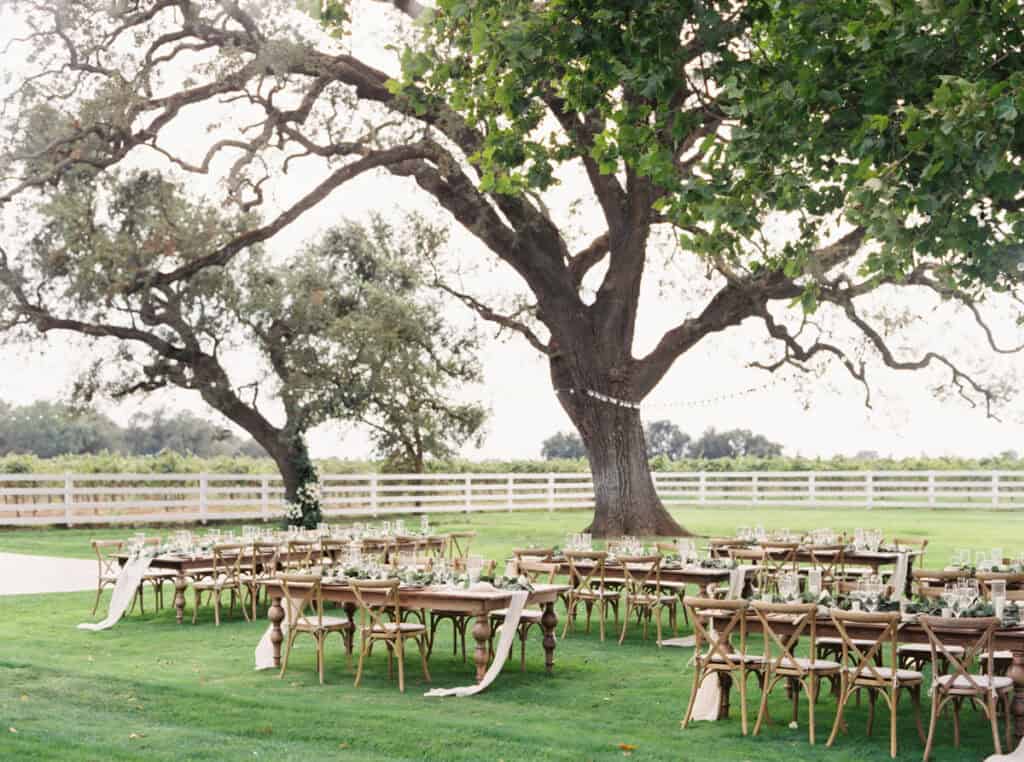 A beautifully arranged reception setup featuring long wooden family-style tables and wooden crossback chairs at a private estate wedding in Lodi, CA.