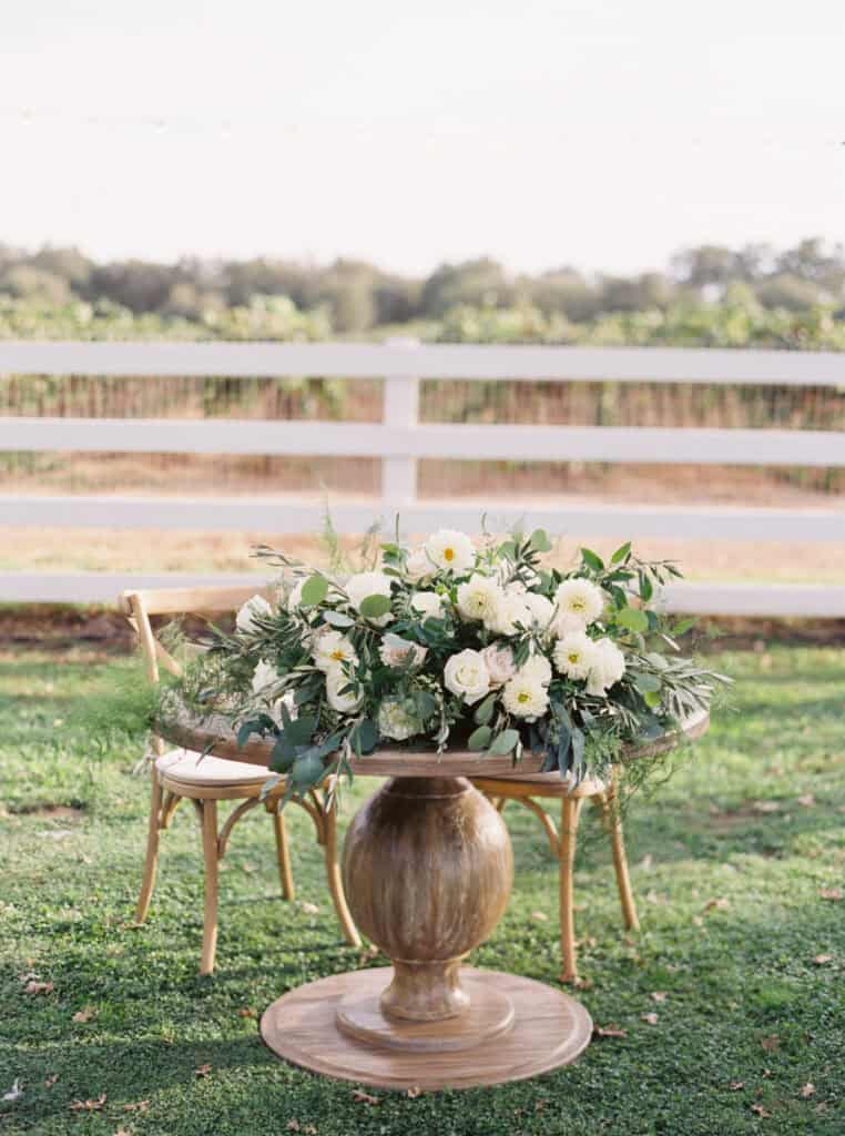 A charming sweetheart table set for the newlyweds, featuring a floral arrangement with white and soft pink flowers, positioned in front of the vineyards at a private estate in Lodi, CA.