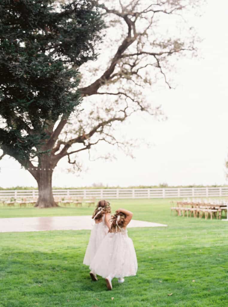 Two flower girls running through a beautifully decorated wedding reception space, filled with joy and laughter.