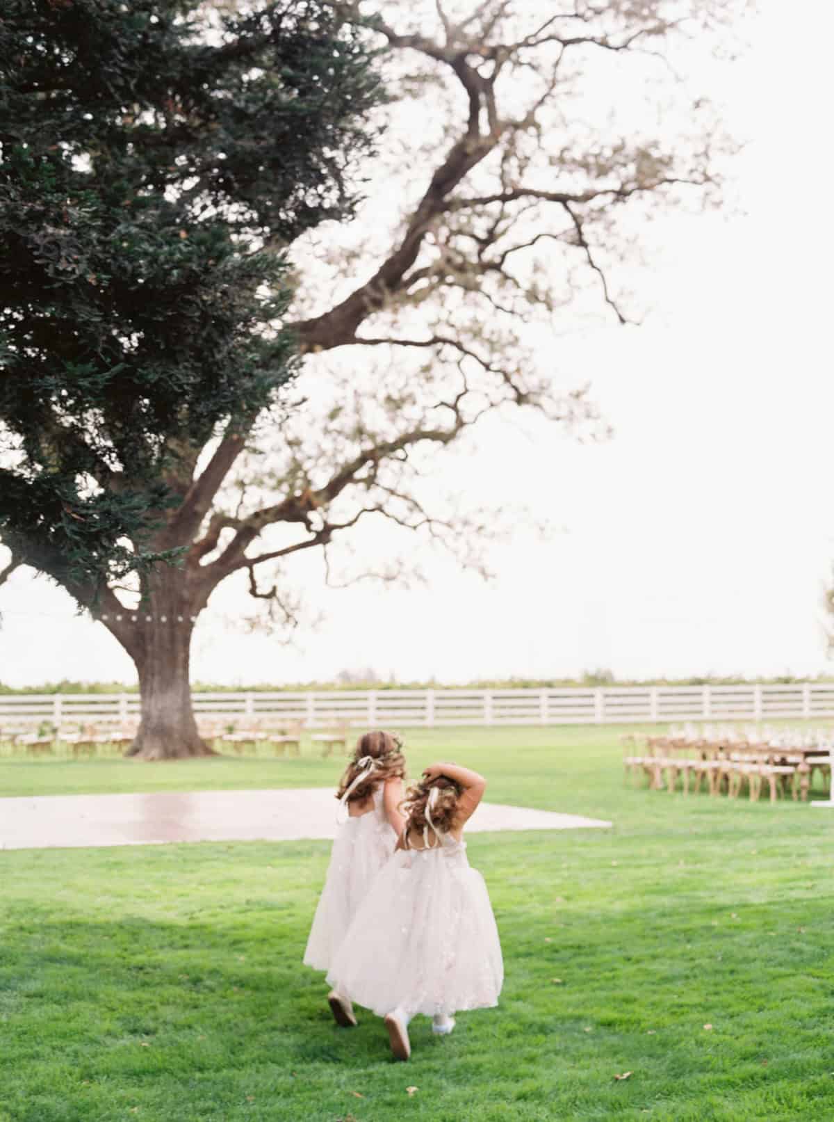 Two flower girls running through a beautifully decorated wedding reception space, filled with joy and laughter.