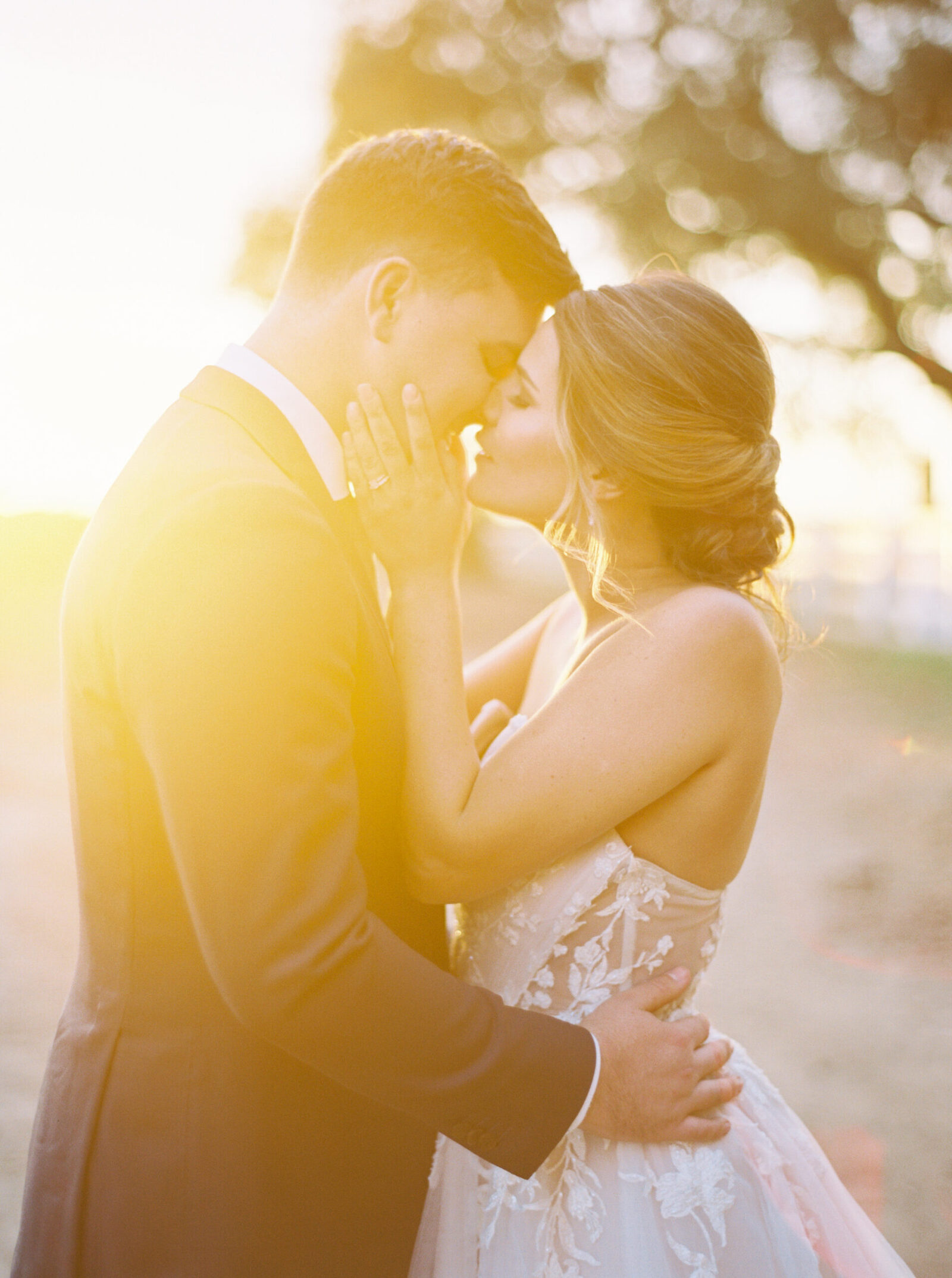 Bride and groom share a romantic kiss bathed in golden sunlight at a private estate wedding.