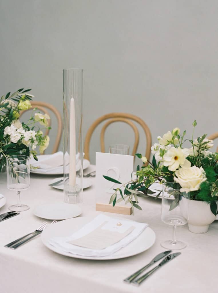 Elegant individual place setting at a wedding reception, featuring a beautifully arranged white floral centerpiece, soft neutral tones, and a refined, timeless design for a sophisticated dining experience.