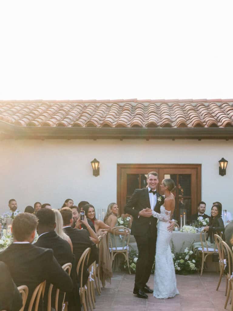 Newlyweds sharing their first dance at the wedding reception, surrounded by guests, as they embrace in a heartfelt moment of joy and celebration.